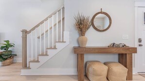 Una escalera con barandillas de madera, una consola de madera con un florero y un espejo, y dos otomanes.