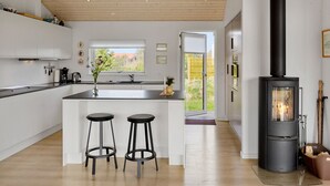 A modern kitchen with a central island, a black wood-burning stove, and a view of the outdoors. - "Minka" - 500m from the sea by Interhome (Blokhus)