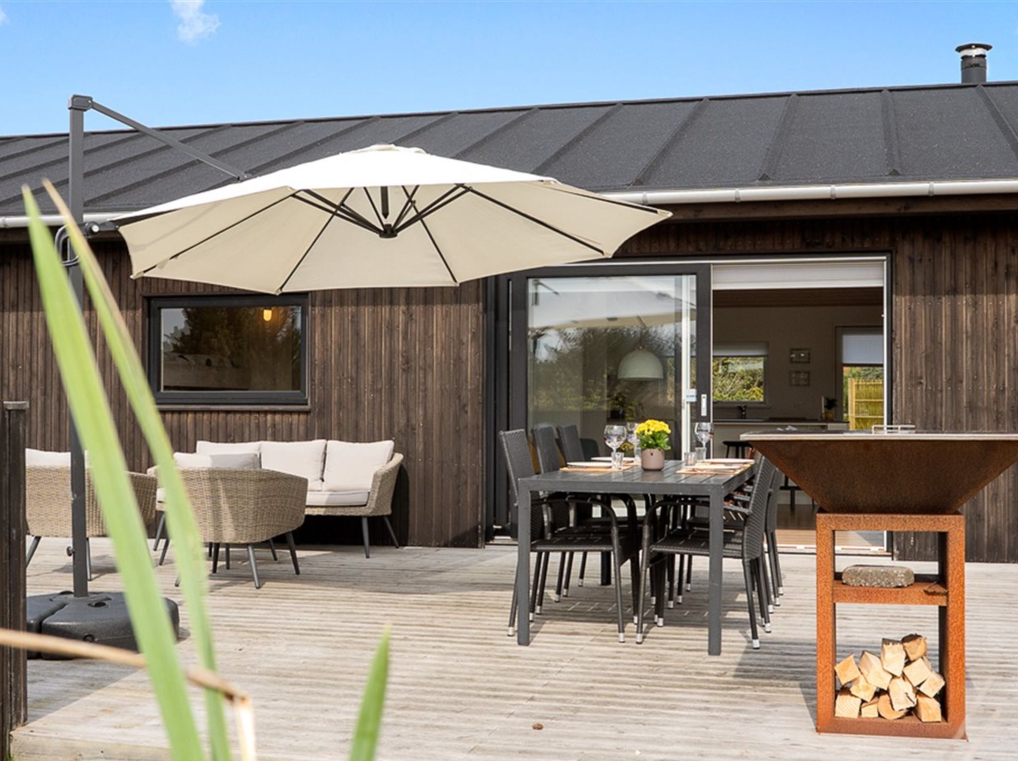An outdoor patio with a table and chairs, a large umbrella, and a wooden deck.