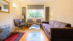 A living room with a sofa, two armchairs, a coffee table, a patterned rug, a mirror, and a window with curtains. - Stylish refurbished flat with private garden, near Regent`s Park (Greater London)