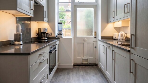 A kitchen with grey cabinets, a black countertop, and a window with frosted glass. - Stylish refurbished flat with private garden, near Regent`s Park (Greater London)