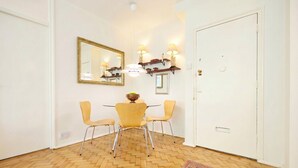 A room with a herringbone wooden floor, a round table with four chairs, a mirror on the wall, and a door with a handle. - Stylish refurbished flat with private garden, near Regent`s Park (Greater London)