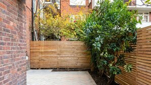A paved patio area with a wooden fence and a brick wall. - Stylish refurbished flat with private garden, near Regent`s Park (Greater London)