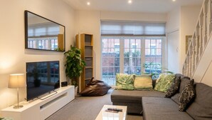 A modern living room with a flat-screen TV, a sofa, a coffee table, and a bookshelf. - Mezzanine loft cottage steps from LGI and the city centre (West Yorkshire)