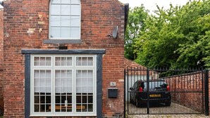 A brick building with a large window, a black metal gate, and a car parked inside. - Mezzanine loft cottage steps from LGI and the city centre (West Yorkshire)