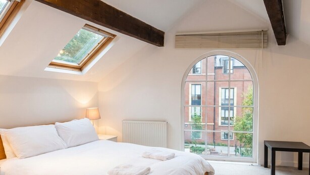 A bedroom with a bed, a skylight, a window, a radiator, and a view of a building. - Mezzanine loft cottage steps from LGI and the city centre (West Yorkshire)