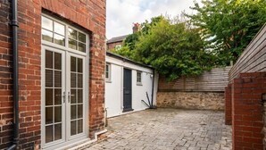 A courtyard with a brick building, a white structure with a door, and a wooden fence. - Mezzanine loft cottage steps from LGI and the city centre (West Yorkshire)