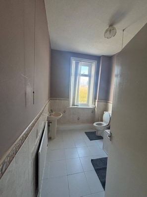 Ein Badezimmer mit Waschbecken, Toilette, Badewanne und einem Fenster mit Blick auf Bäume.