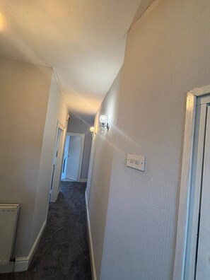 A narrow hallway with a carpeted floor, a light switch, and a wall-mounted light fixture. - Room-serene Ocean View Apartment Room in (Sunderland)