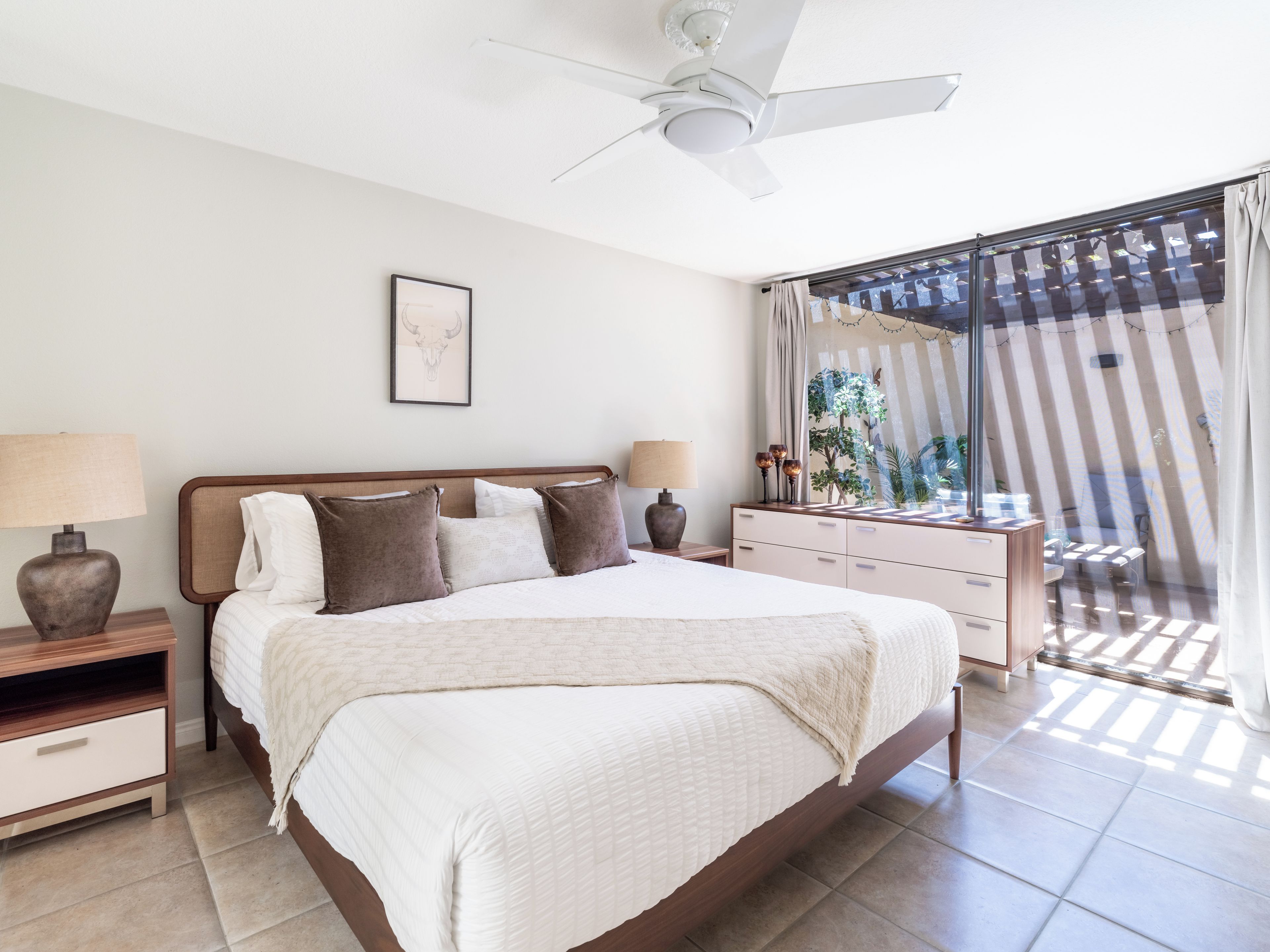 A bedroom with a bed, bedside tables, a ceiling fan, and a view of the outdoors.