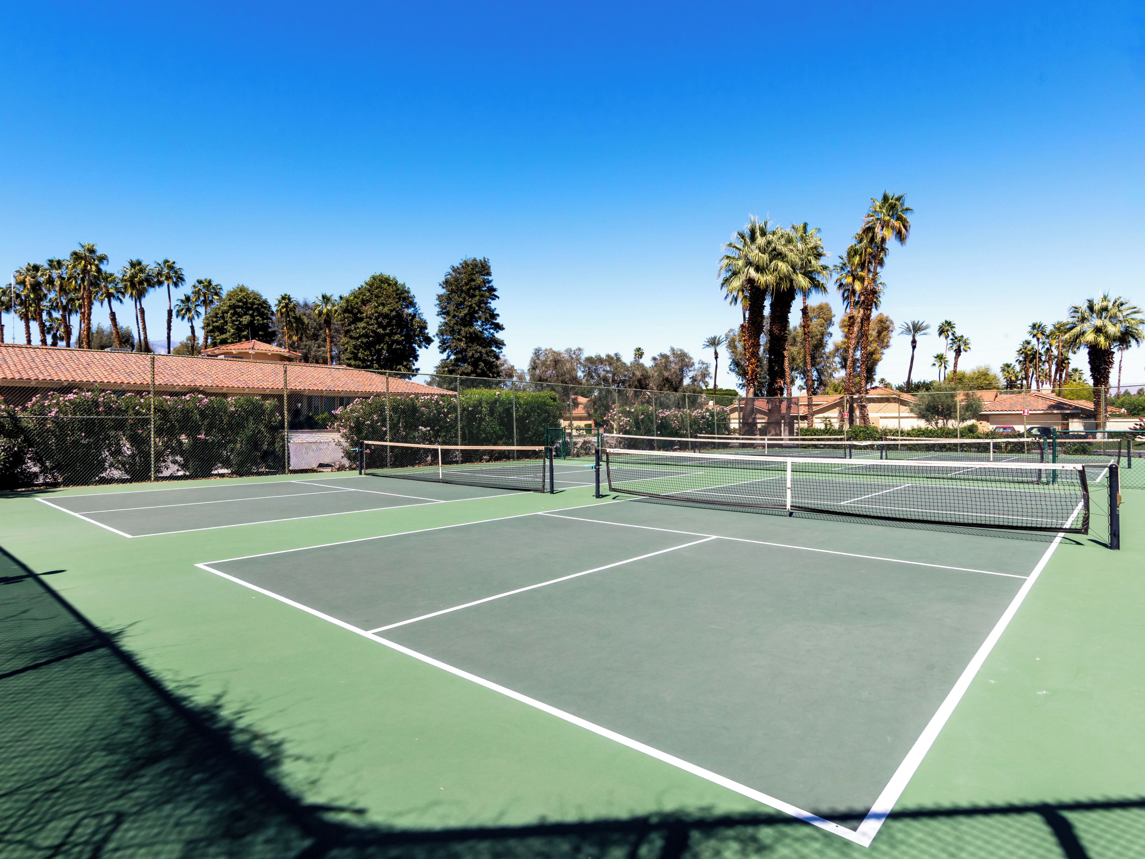 A tennis court with a net, surrounded by trees and a building with a red roof.