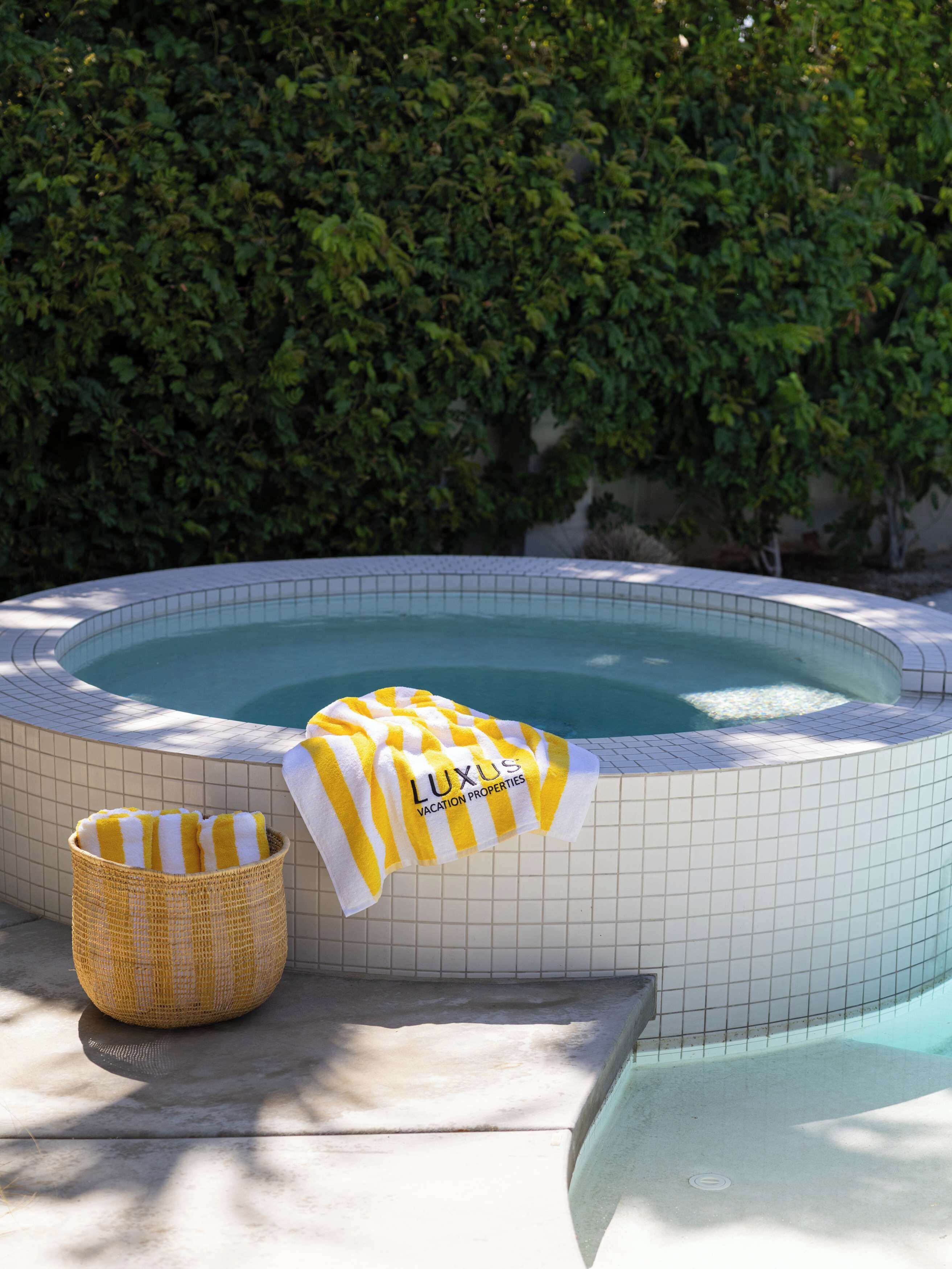 Een jacuzzi met betegelde rand, een gele en witte streephanddoek en een rieten mand.