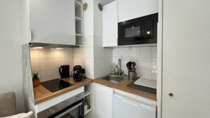 Een compacte keuken met witte kastjes, een magnetron, een koffiezetapparaat en een spoelbak.