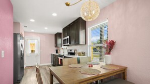 A modern kitchen with dark cabinets, a stainless steel refrigerator, and a dining area with a wooden table and benches. - Opalite on Sunset | Pink Beach Retreat (Panama City Beach)