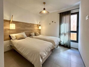 A bedroom with two beds, a wooden headboard, a window with curtains, and a hanging light fixture. - 4th floor, terrace, tv, 80m², Serre Chevalier (Briançon)