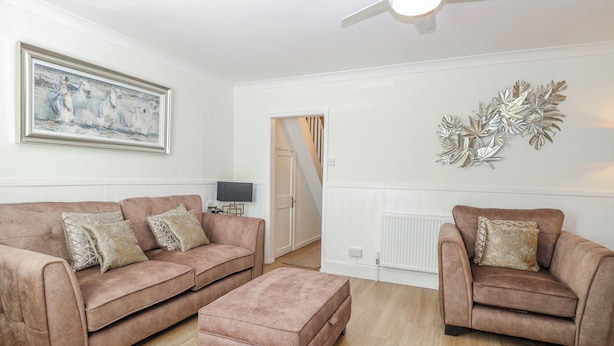 Een woonkamer met twee banken, een poef, een plafondventilator, een radiator en een decoratief object aan de muur.