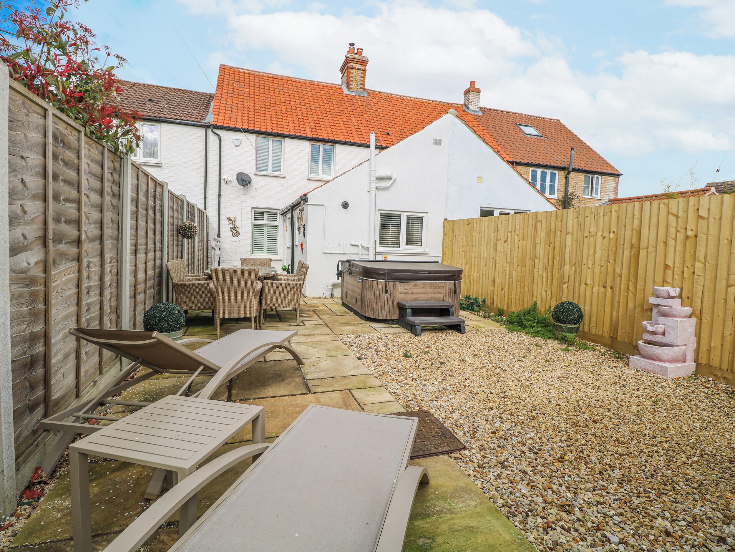 A backyard with a patio, outdoor seating, a hot tub, and a wooden fence.