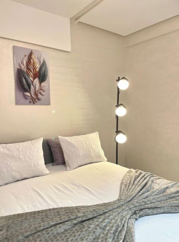 Un lit bien fait, avec des oreillers, une œuvre d’art accrochée au mur et une lampe de chevet.