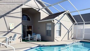 Piscina com estrutura de toldo, área de varanda coberta com cadeiras e entrada de um edifício.