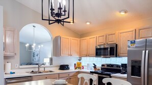 Uma cozinha moderna com armários de madeira, eletrodomésticos de aço inoxidável, uma ilha central com bancos e um lustre.