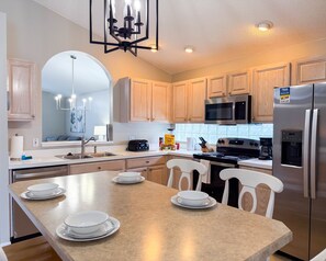 A modern kitchen with wooden cabinets, stainless steel appliances, a central island with seating, and a chandelier. - Ridgewood Lakes - 3 bedrooms Pool Home with Game Room (Davenport)
