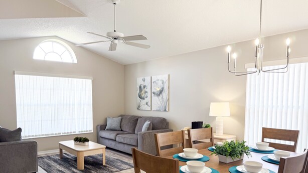 Uma sala de estar moderna com área de jantar, ventilador de teto e uma grande janela com persianas.