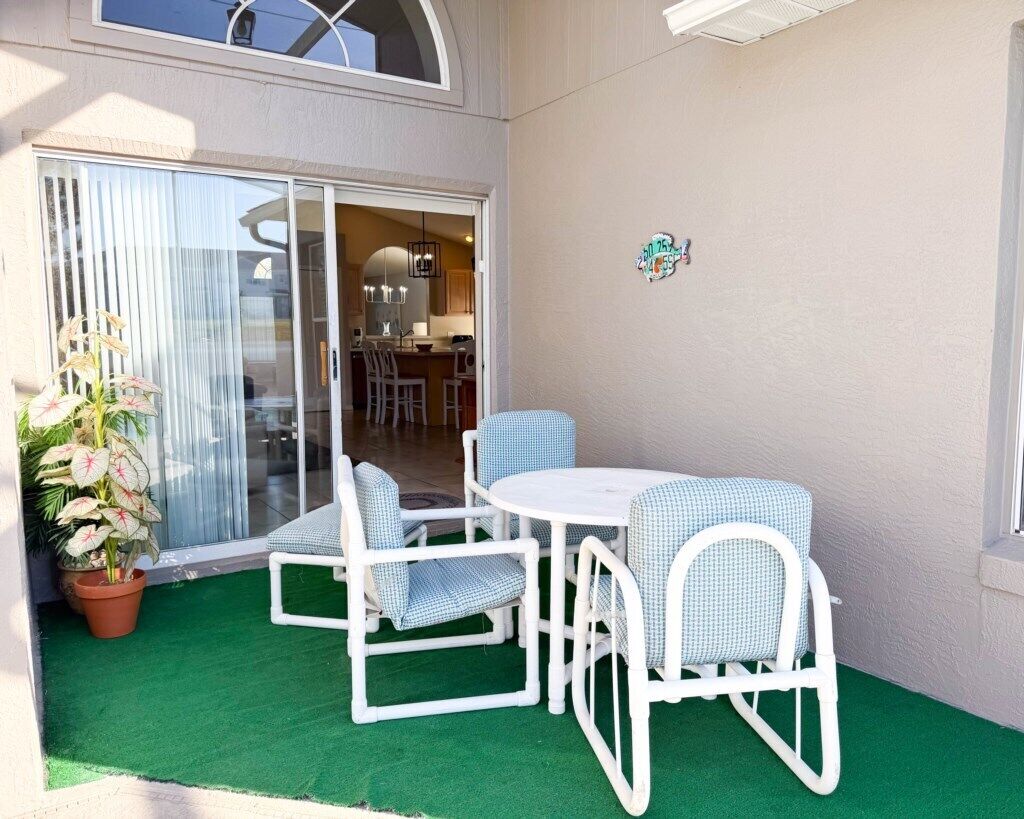 Un patio con una mesa, sillas, una planta en maceta y un cerramiento de vidrio corredera que da a un espacio interior.