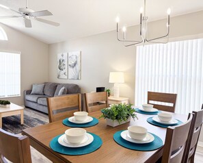 A modern dining room with a wooden table set for four, a ceiling fan, and a chandelier. - Ridgewood Lakes - 3 bedrooms Pool Home with Game Room (Davenport)