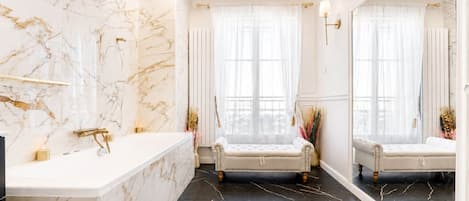 Ein Badezimmer mit Marmorwand, schwarzem Fliesenboden, freistehender Badewanne und großem Spiegel.