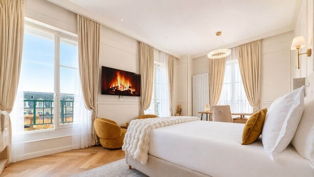 Ein Hotelzimmer mit einem großen Bett, einem Schreibtisch, einem Sessel und einem Fernseher, der einen Kamin zeigt, sowie Blick auf die Stadt.
