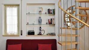 A red sofa with cushions, a glass shelf with books and decorative items, and a spiral staircase with wooden steps. - Residenza Le Sirene - Holiday Home with Jacuzzi and Terrace near Tropea (Santa Domenica)