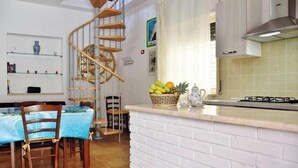 A kitchen with a white brick backsplash, a wooden spiral staircase, and a dining area with a blue tablecloth. - Residenza Le Sirene - Holiday Home with Jacuzzi and Terrace near Tropea (Santa Domenica)