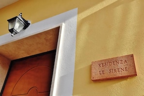 Eine Tür mit kreisförmigem Design, eine Wandleuchte und eine Schilder mit der Aufschrift 'RESIDENZA LE SIRENE'.