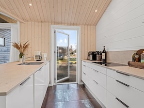 Een moderne keuken met een schuifdeur naar een terras, witte kasten en een koffiezetapparaat op het aanrecht.