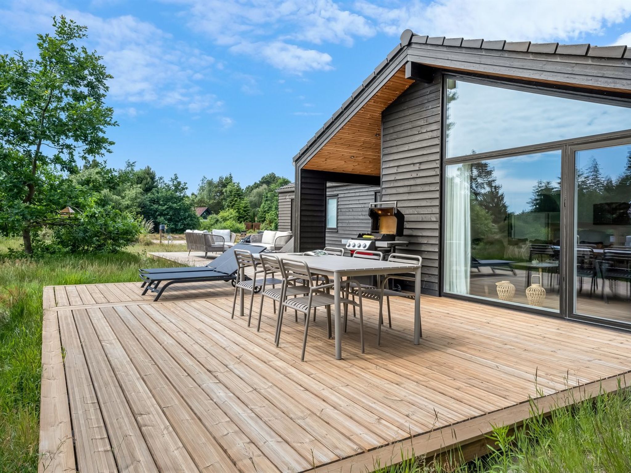 A modern outdoor deck with a dining area, a grill, and a glass-enclosed patio.