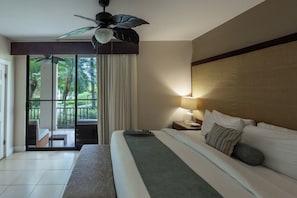 Ein Hotelzimmer mit Bett, Nachttisch, Lampe, Deckenventilator und Blick auf Grün hinter einer Schiebetür.