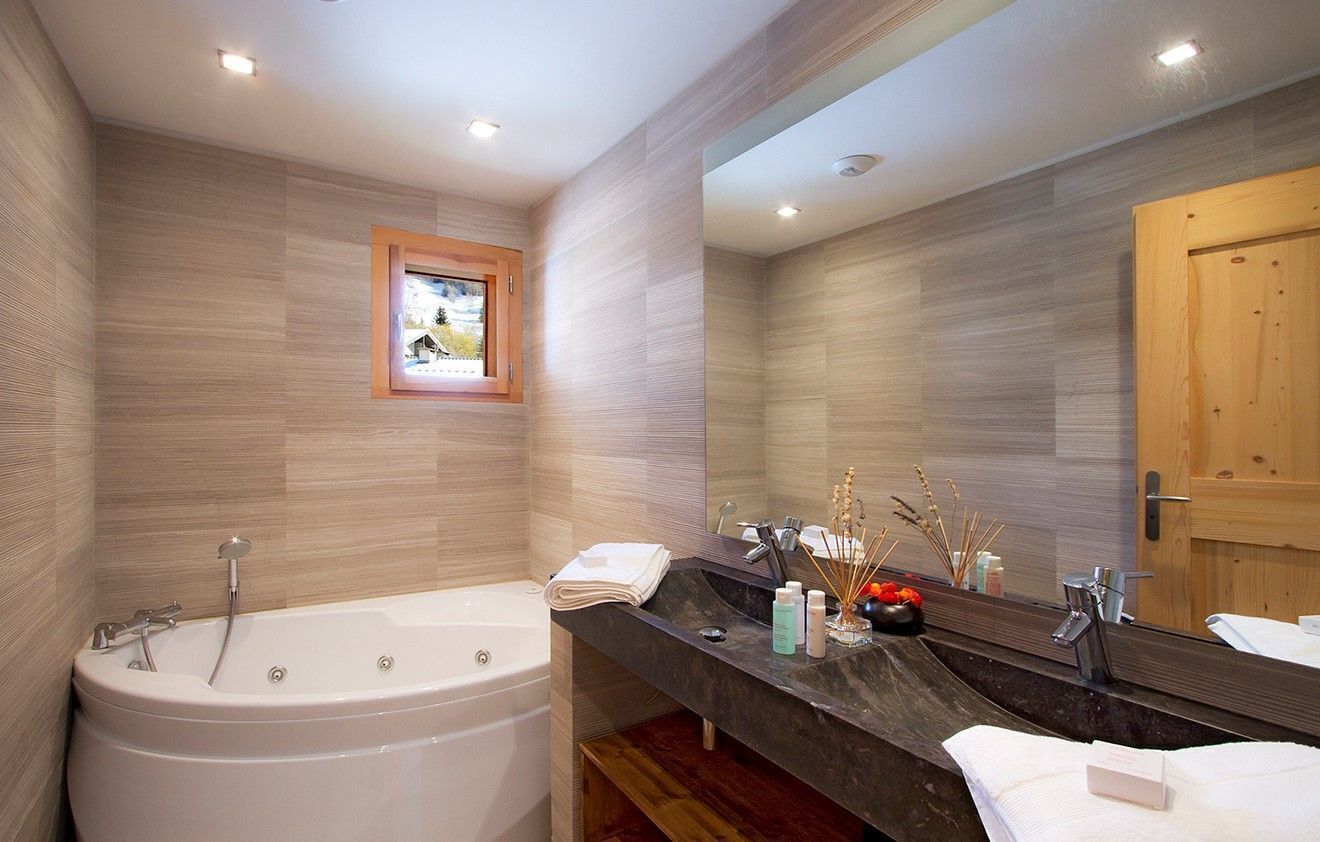 A modern bathroom with a freestanding bathtub, a large mirror, and a wooden door.