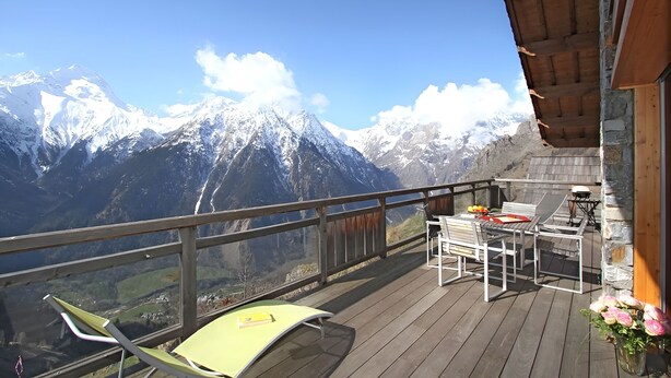 Un balcone con un pavimento in legno, arredi da esterno e vista sulle montagne innevate.