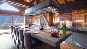 Una cucina moderna con isola centrale, travi in legno e ampie finestre con vista su un paesaggio montuoso.