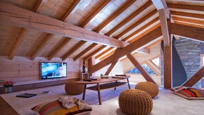 Una camera mansardata accogliente con travi in legno, televisione, un tavolo e due pouf lavorati a maglia.