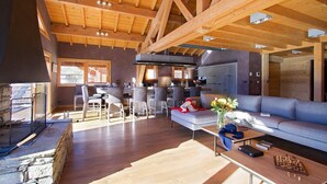 Un'ampia zona giorno con soffitto in legno a vista, camino e cucina moderna sullo sfondo.