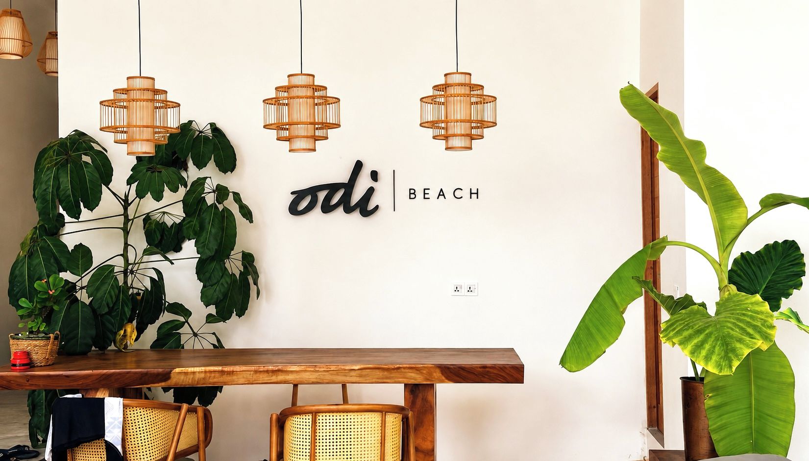 A dining area with a wooden table, wicker chairs, hanging wicker pendant lights, and large green plants.