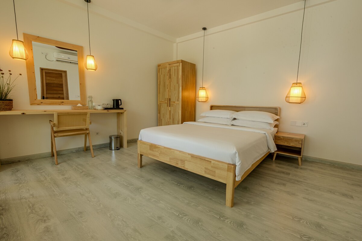A bedroom with a wooden bed, a bedside table, a chair, a wardrobe, and a desk with a mirror.