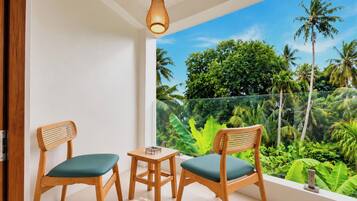 A balcony with two wooden chairs and a small table, overlooking a lush tropical garden.