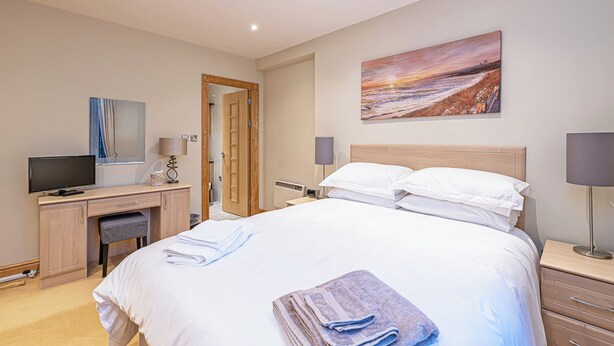 Ein Hotelzimmer mit einem Bett, einem Schreibtisch mit Computer, einem Fernseher und einem Bild an der Wand.