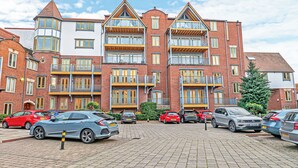 Ein mehrgeschossiges Wohngebäude mit Ziegelverkleidung, mehreren Balkonen und einem Parkplatz mit verschiedenen Autos.