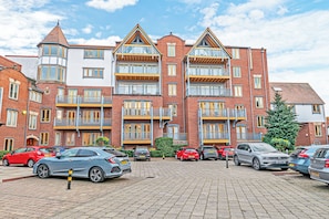 A multi-story residential building with a brick facade, multiple balconies, and a parking area with various cars. - Foregate Apartment by Guestz (Chester)