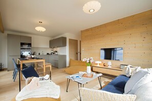 A modern living room with a sofa, coffee table, and a TV mounted on a wooden wall. - Vue sur les pistes, ski aux pieds, T3 + cabine (Alpe d'Huez)