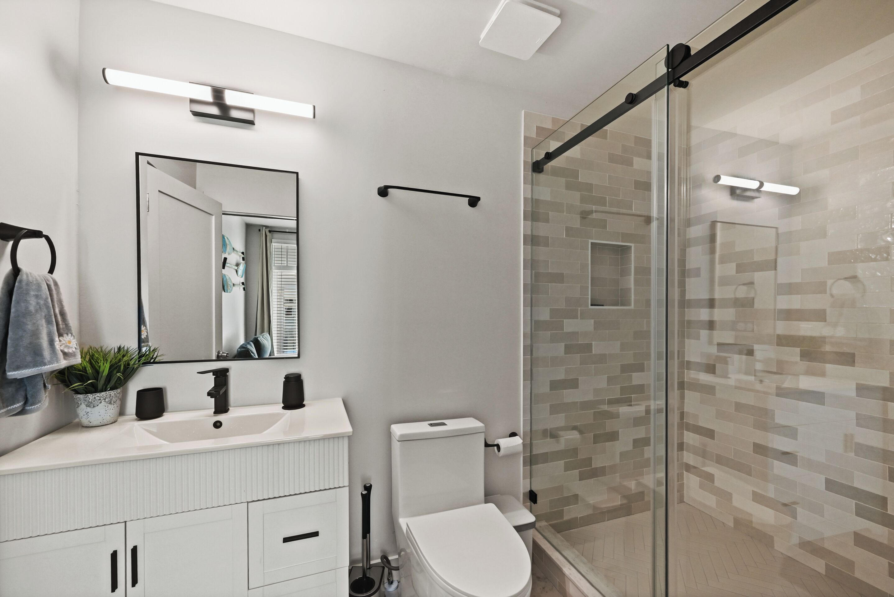 A modern bathroom with a white sink, mirror, and toilet, a glass shower enclosure, and a tiled shower wall.