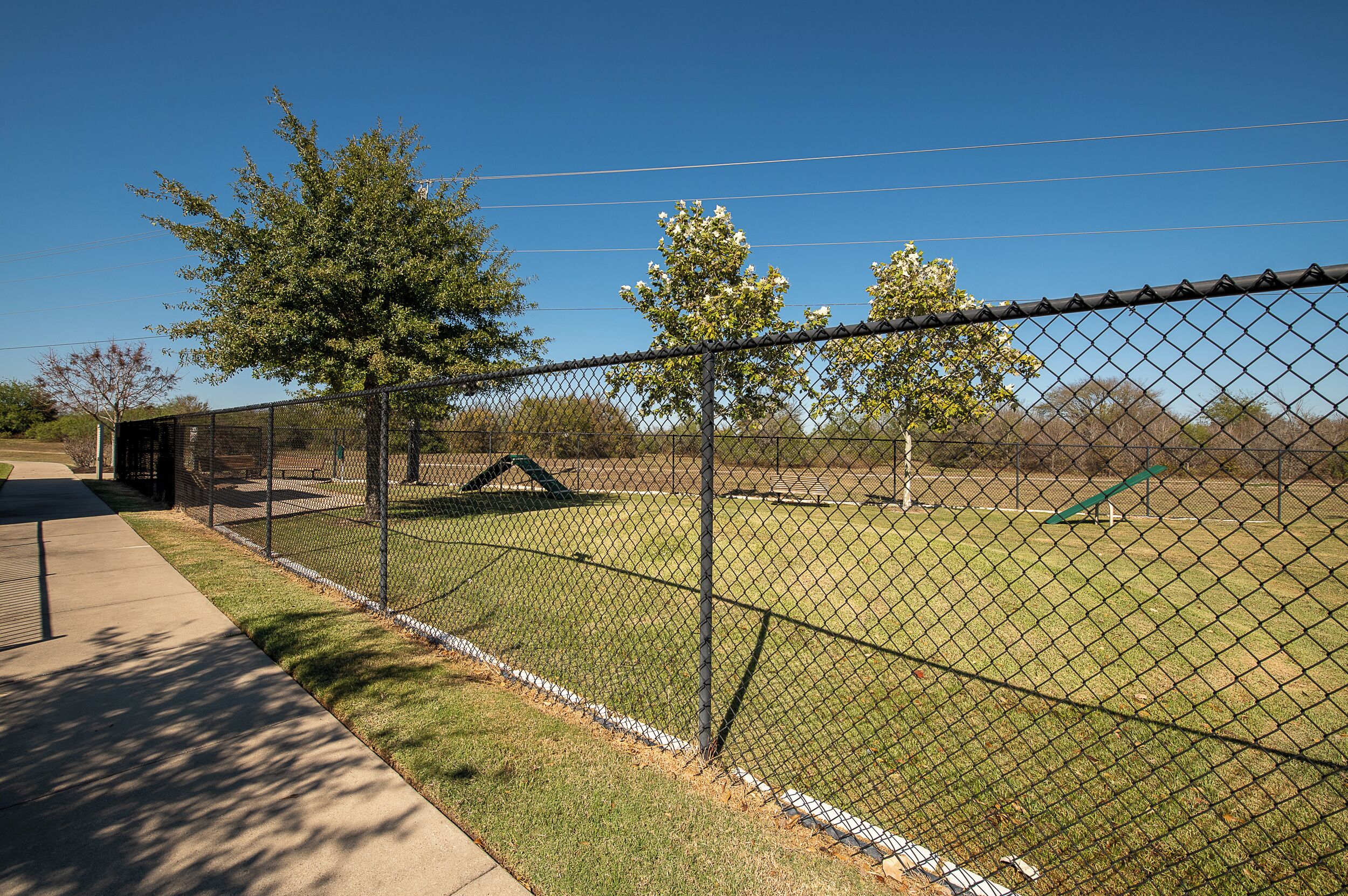 A fenced outdoor area with a grassy field, trees, and a playground.